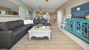 A living room with a dark gray sectional sofa, a white coffee table with decorative items, a teal cabinet, and a ceiling fan. - GULF VIEWS IN A  PREMIER RESORT!! GREAT RATES! (Destin)