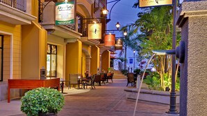 Un patio interior con un banco, mesas, sillas y letreros colgantes para Dolce Vita Coffee y Dolce Vita Sweets.