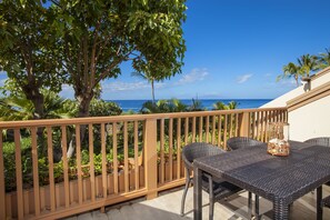 Een balkon met een rieten tafel en stoelen, met uitzicht op zee en palmbomen.