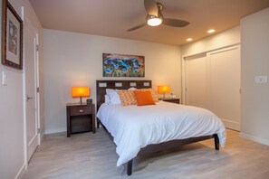 A bedroom with a bed, two bedside tables, a ceiling fan, and a painting on the wall.