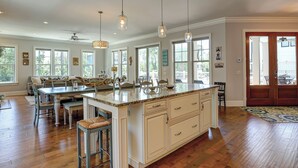 Une cuisine spacieuse dotée d’un grand îlot central, de luminaires suspendus et offrant une vue sur l’extérieur grâce à de grandes fenêtres.