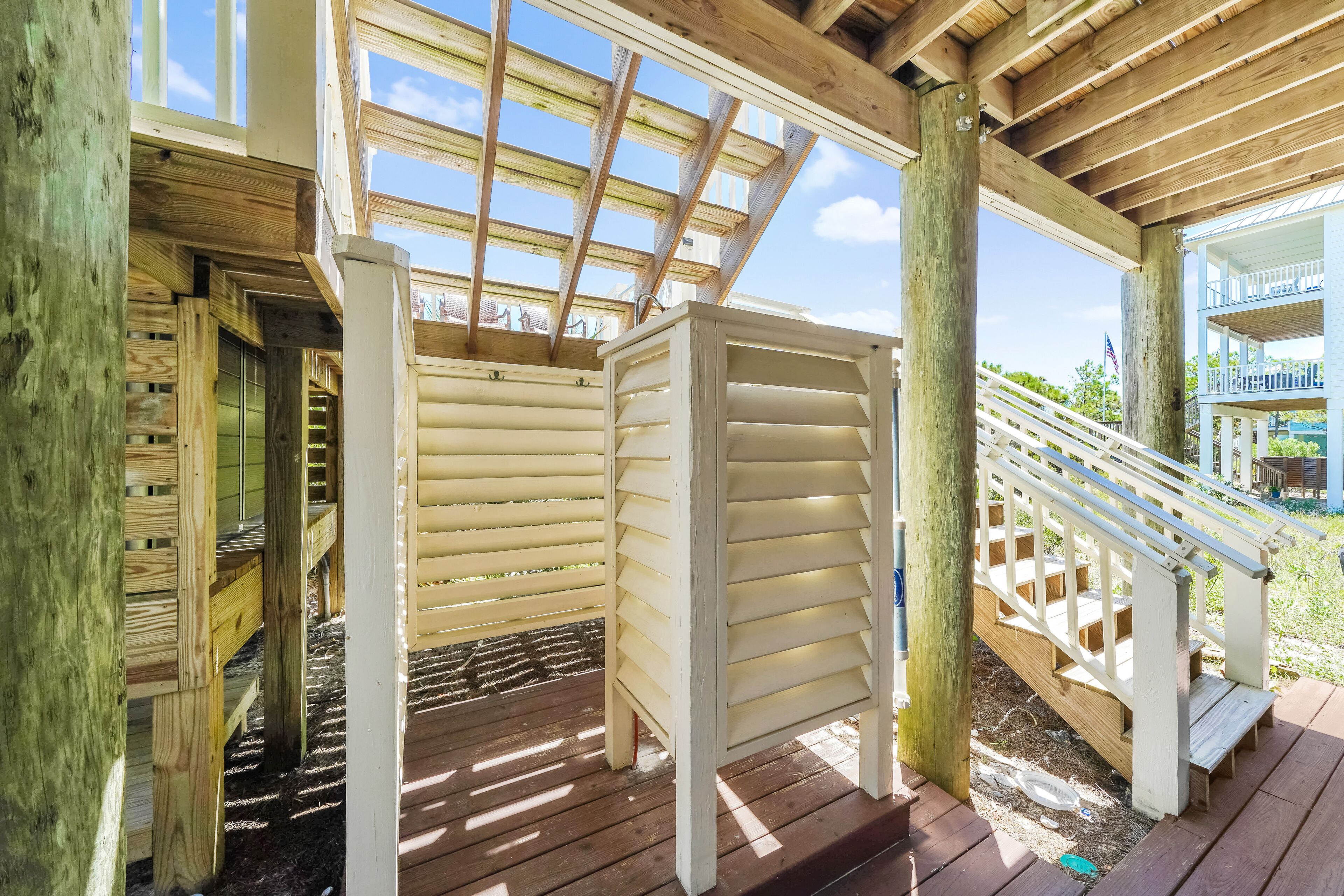 A wooden deck with a covered area, wooden railings, and a staircase leading to an upper level.