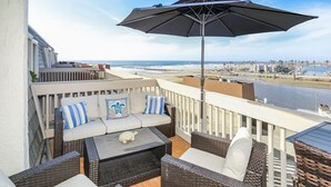 A balcony with wicker furniture, a sofa with cushions, and a large umbrella. - Awesome Sunset Ocean Views, Huge deck with Beautiful Ocean/Harbor Views, G317 North Coast Village (Oceanside)