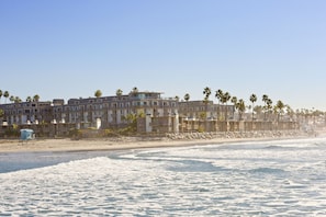 A beachfront hotel with multiple floors, balconies, and palm trees. - Awesome Sunset Ocean Views, Huge deck with Beautiful Ocean/Harbor Views, G317 North Coast Village (Oceanside)