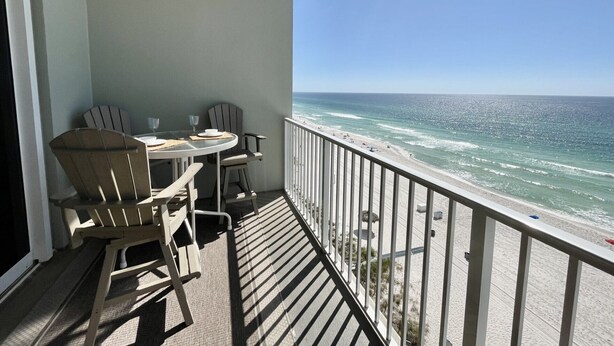 Un balcon avec une table et des chaises, donnant sur une plage où l’on peut admirer les vagues et un ciel dégagé.