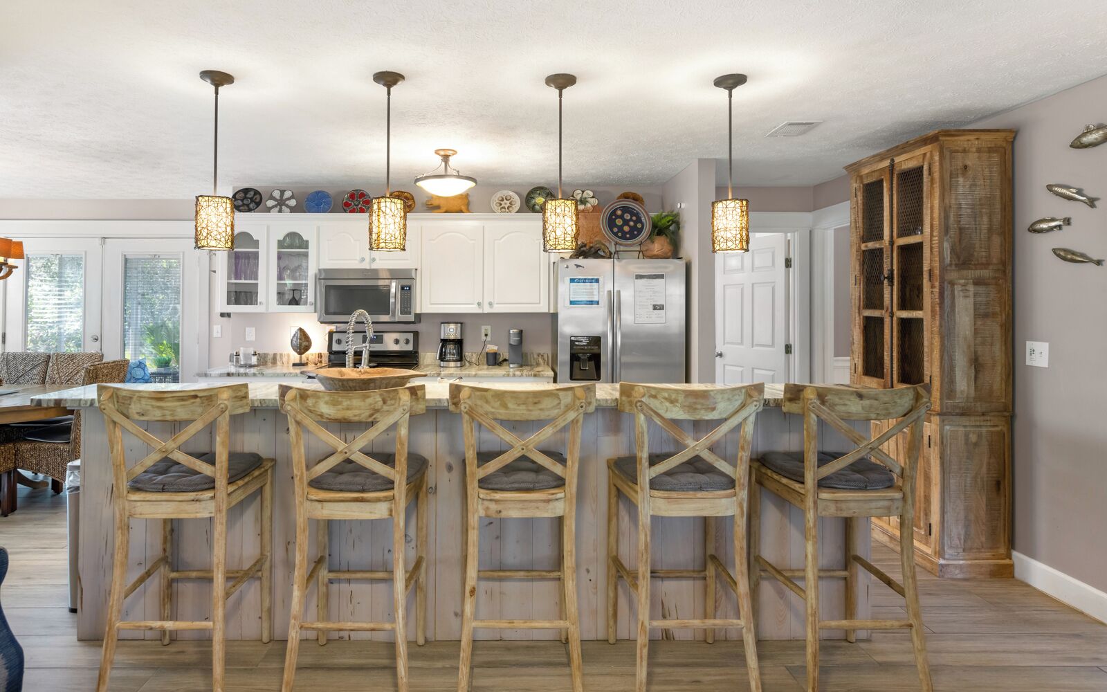 Una cocina con una isla central, taburetes de bar, lámparas colgantes y un armario de madera.