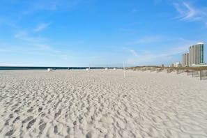 Een strand met een volleybalnet, een zandstrand en een hoog gebouw op de achtergrond.