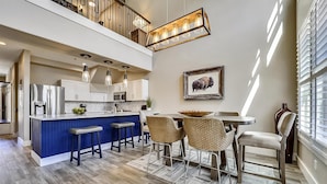 Une cuisine moderne avec un îlot central bleu, des appareils en acier inoxydable et un coin repas agrémenté de chaises en osier et d’une table ronde.