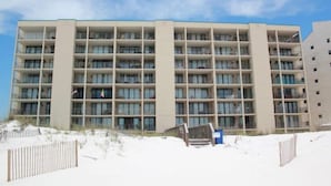 Ein mehrstöckiges Hotel mit einheitlicher Fassade, Balkonen und einem sandigen Vordergrund.