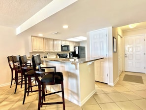 A modern kitchen with a central island, bar stools, and white cabinetry.
