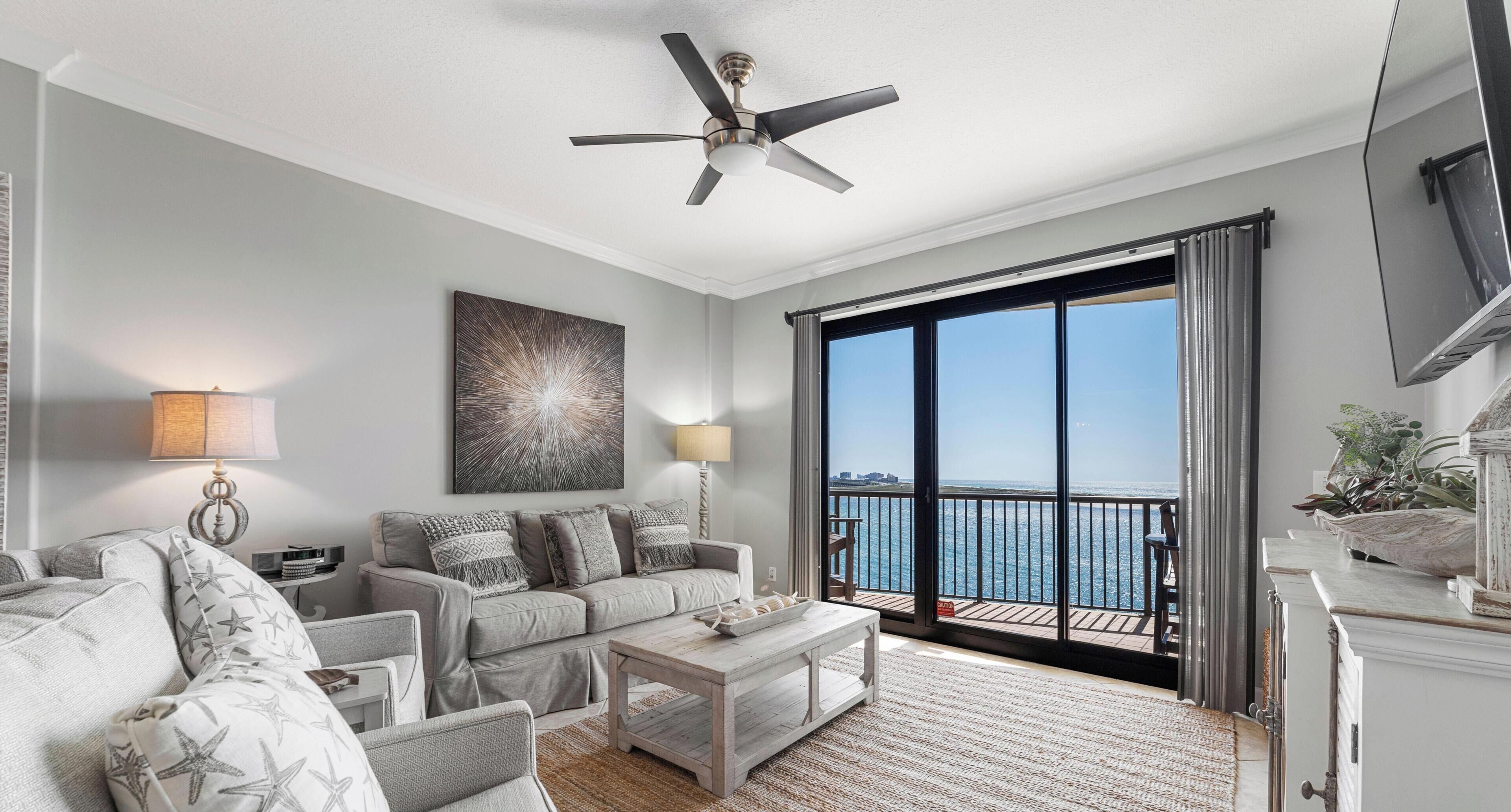 A living room with a sofa, coffee table, and artwork. There is a balcony with a view of the sea.