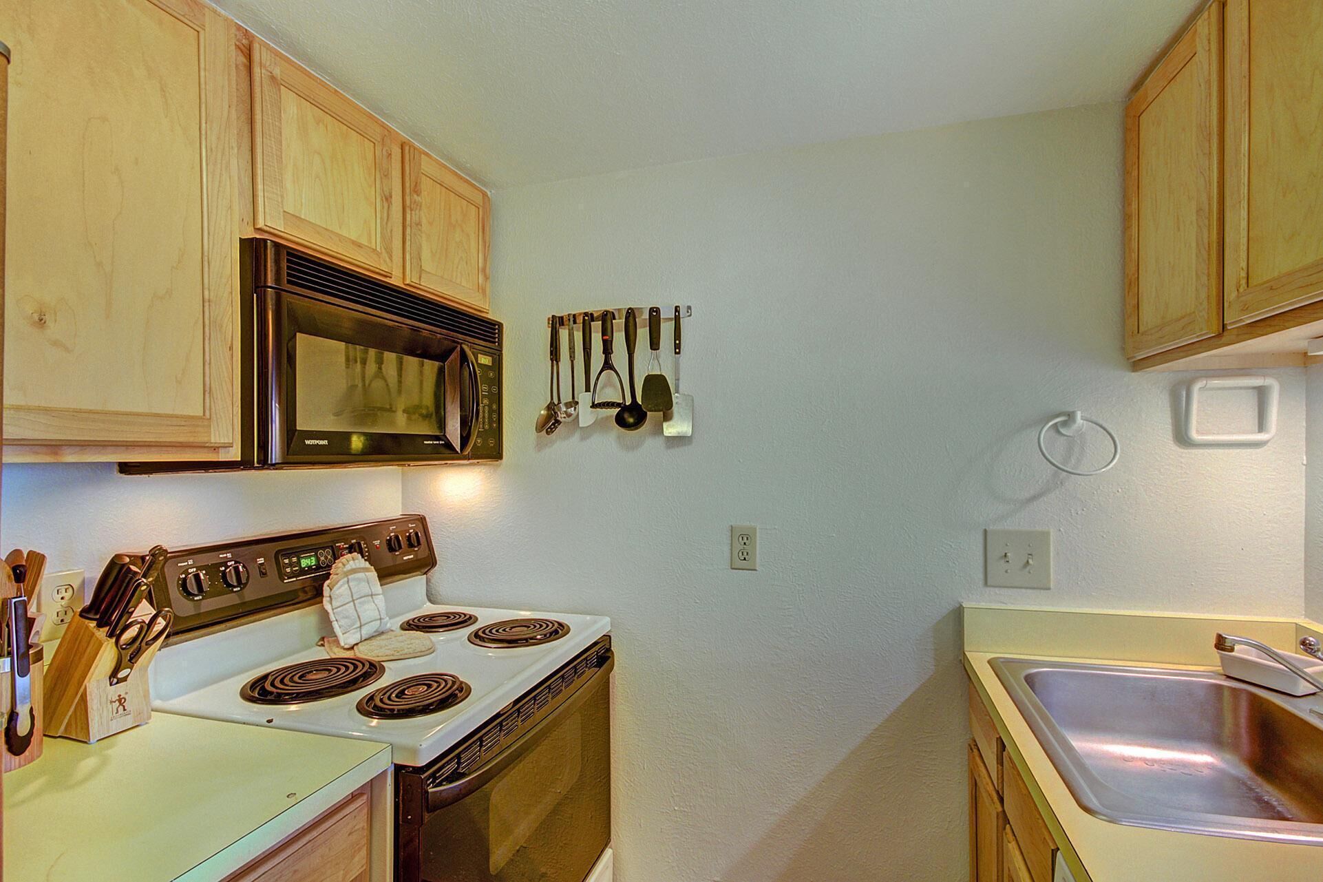 A compact kitchen with wooden cabinets, a microwave, a stove, and a sink.