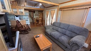 A compact living space with a sofa, a wooden table, a rocking chair, and a kitchenette area.