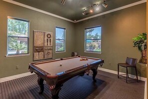 Een pooltafel in een kamer met grote ramen, een stoel en een kunstwerk aan de muur.