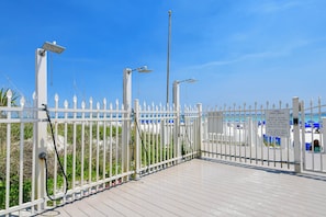 A gated beach area with a white picket fence, a sign indicating wristband and security key requirements, and a clear blue sky. - Tropical beachfront getaway w/ private balcony and amenities! (Destin)