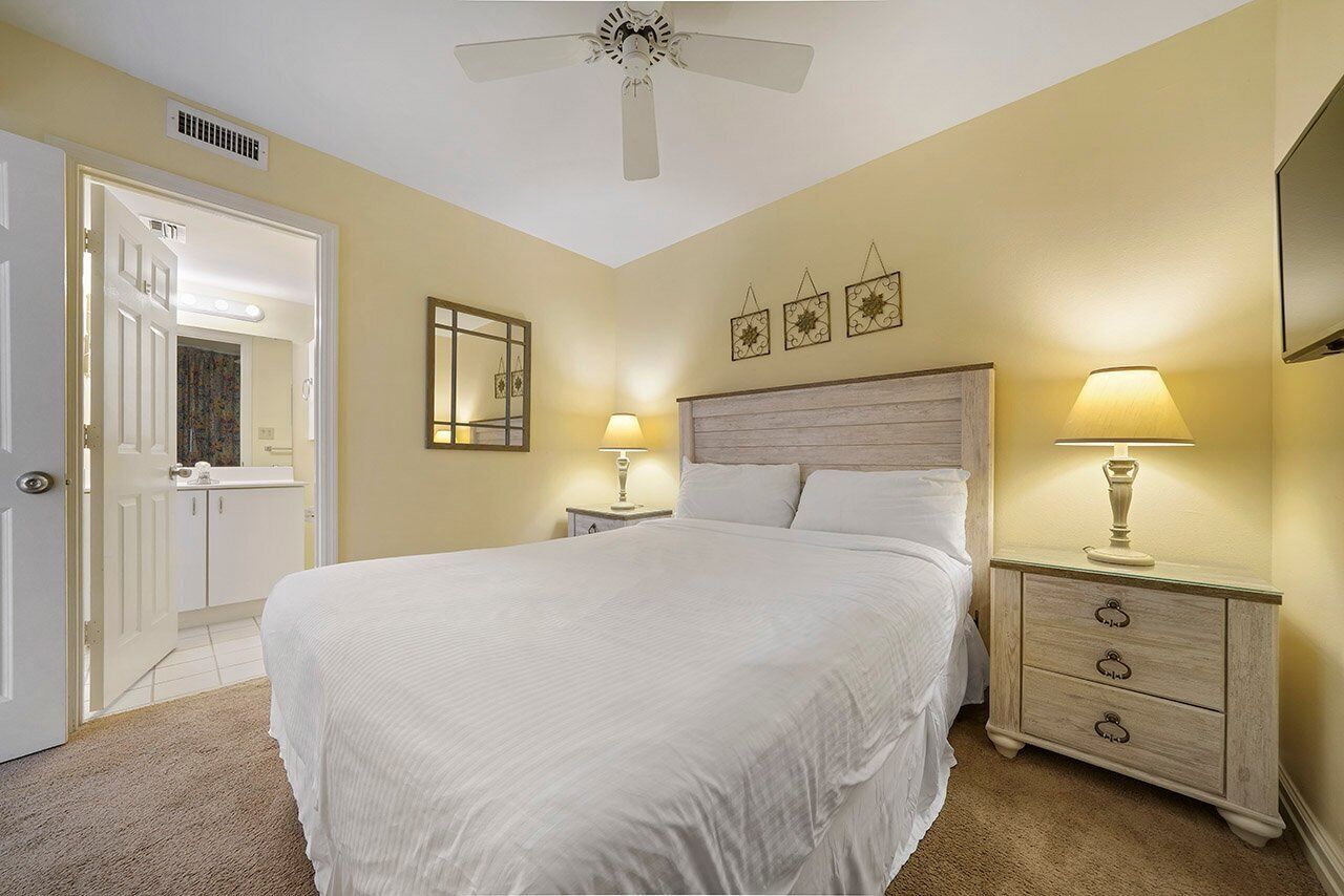 A bedroom with a large bed, bedside lamps, a ceiling fan, and a door leading to a bathroom.