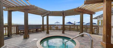 A wooden deck with a hot tub, benches, and umbrellas.