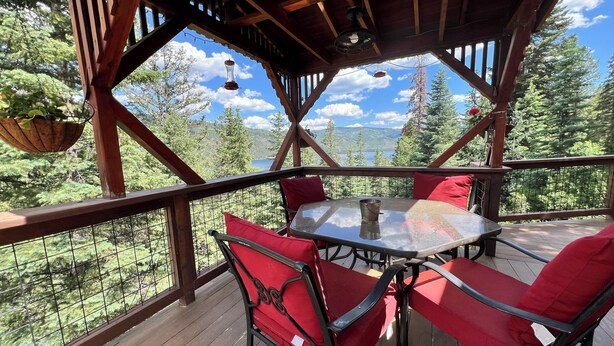 Una terraza de madera con una mesa redonda y sillas rojas, con vistas a una zona boscosa y montañas a lo lejos.