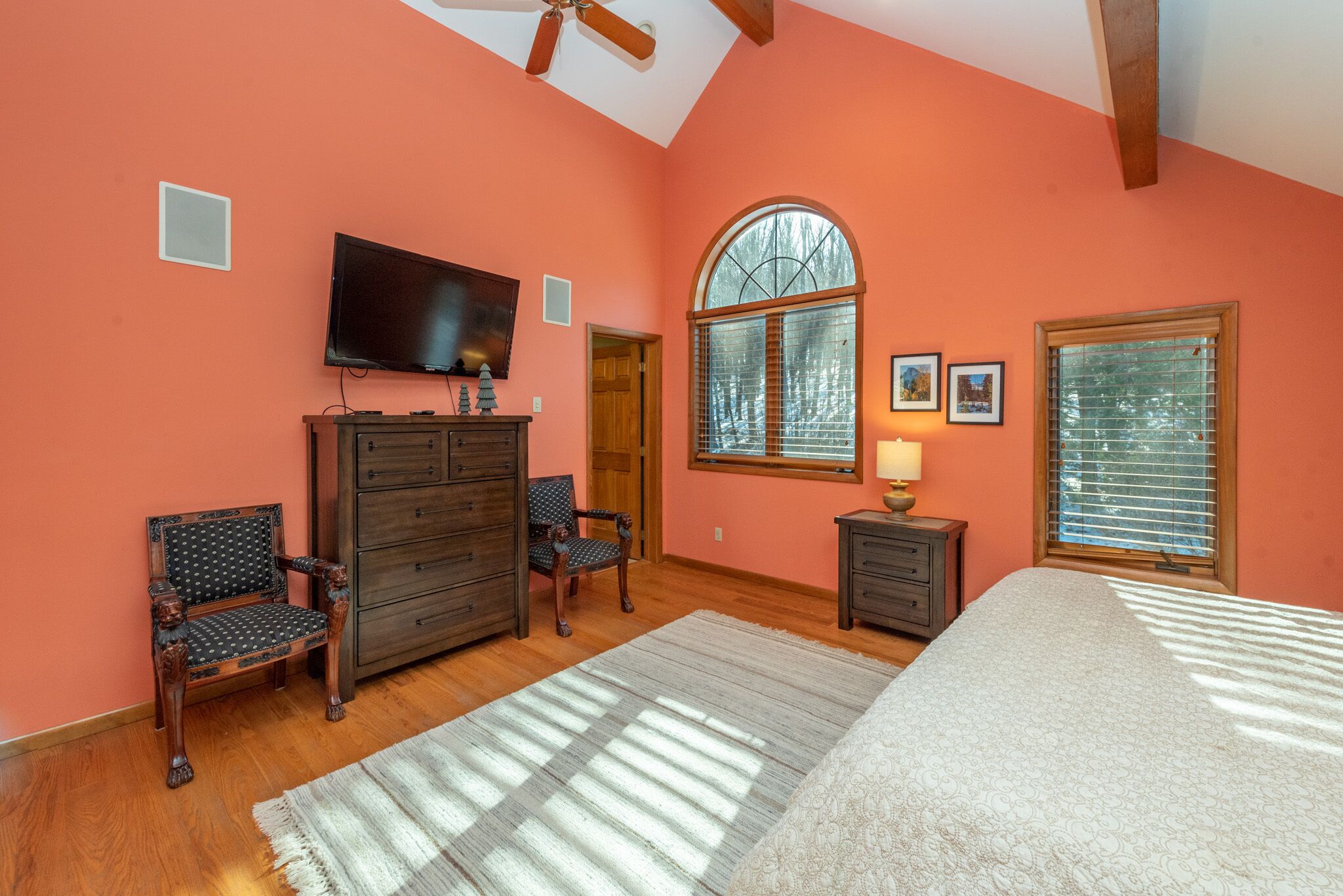 Une chambre à coucher avec un grand lit, une commode, un téléviseur et une fenêtre avec des stores.
