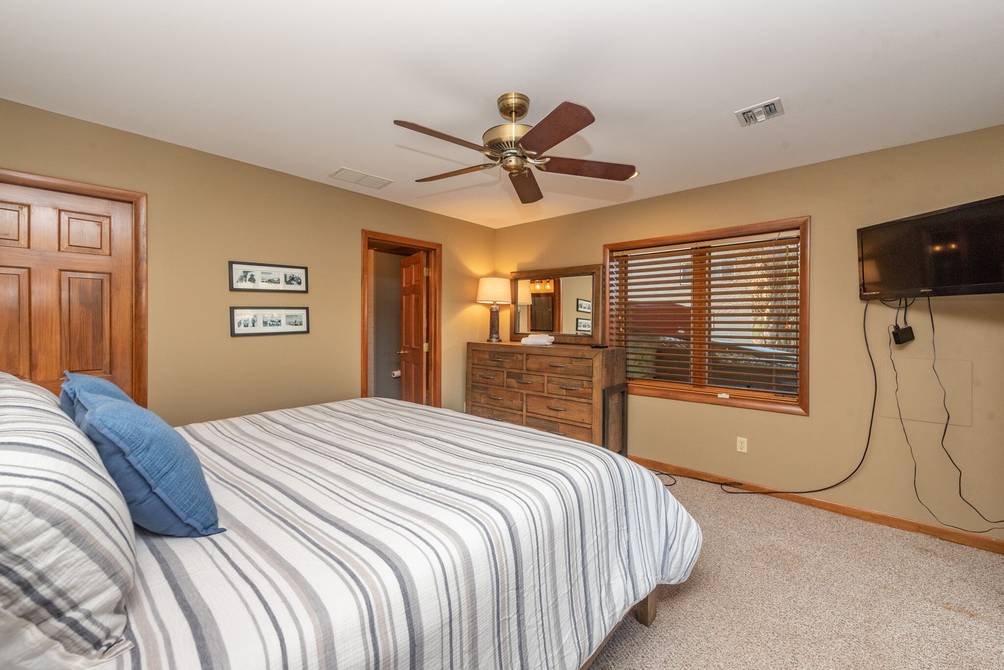 A bedroom with a bed, a dresser, a ceiling fan, a television, and wall-mounted artwork.