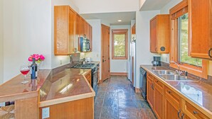 A kitchen with wooden cabinets, a granite countertop, and a view through an open door to a garden. - LYNX AT THE TERRACES- Slopeside Ski-In/Ski-Out Condo in the Meadows of Mountain (Mountain Village)