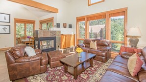 A spacious living room with leather sofas, a wooden coffee table, and a fireplace. Large windows offer a view of the outdoors. - LYNX AT THE TERRACES- Slopeside Ski-In/Ski-Out Condo in the Meadows of Mountain (Mountain Village)