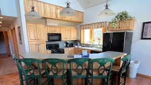 A kitchen with wooden cabinets, a central island with chairs, a stove, and a refrigerator.