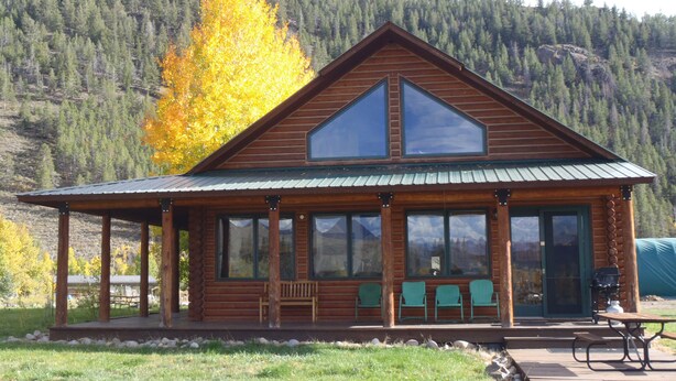 A log cabin with a porch, large windows, and a view of a forested mountain.