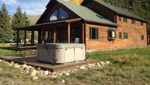 A log cabin with a covered porch, a hot tub, and a view of a forested mountain.