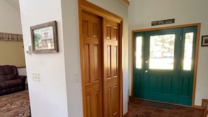 A hallway with a wooden door, a green door with a sign, a framed picture on the wall, and a brown couch.