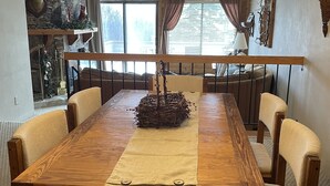 Uma sala de jantar com mesa de madeira, cadeiras bege, um candelabro e uma lareira de pedra.
