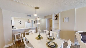 A compact kitchen with white cabinets, a refrigerator, and a dining area with a white table set for two.