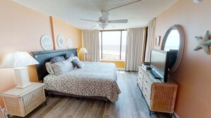 A bedroom with a bed, a television, a ceiling fan, and a window with curtains.