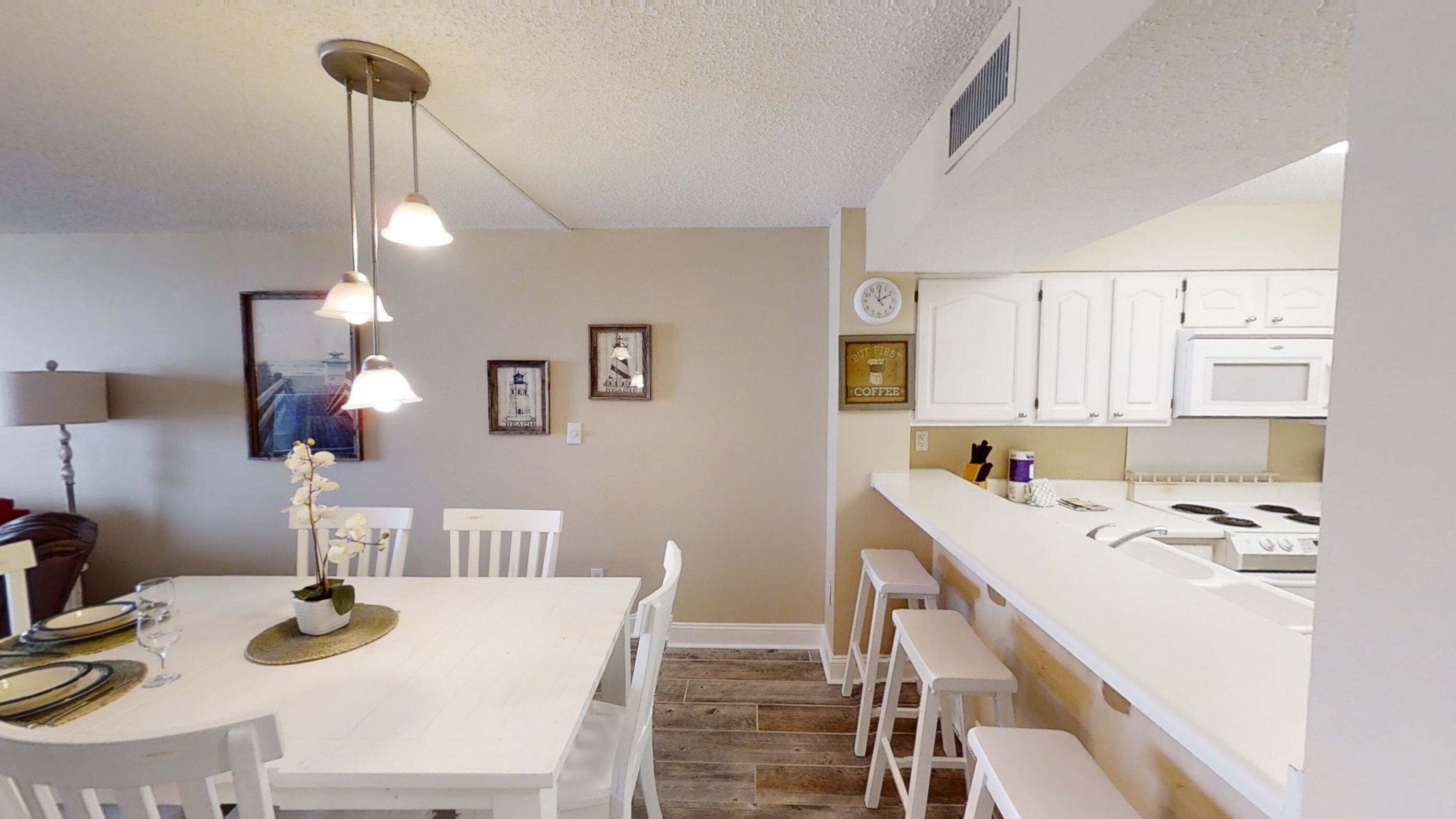 Un coin repas avec une table et des chaises blanches, un luminaire suspendu, et une cuisine avec des armoires et des appareils électroménagers blancs.