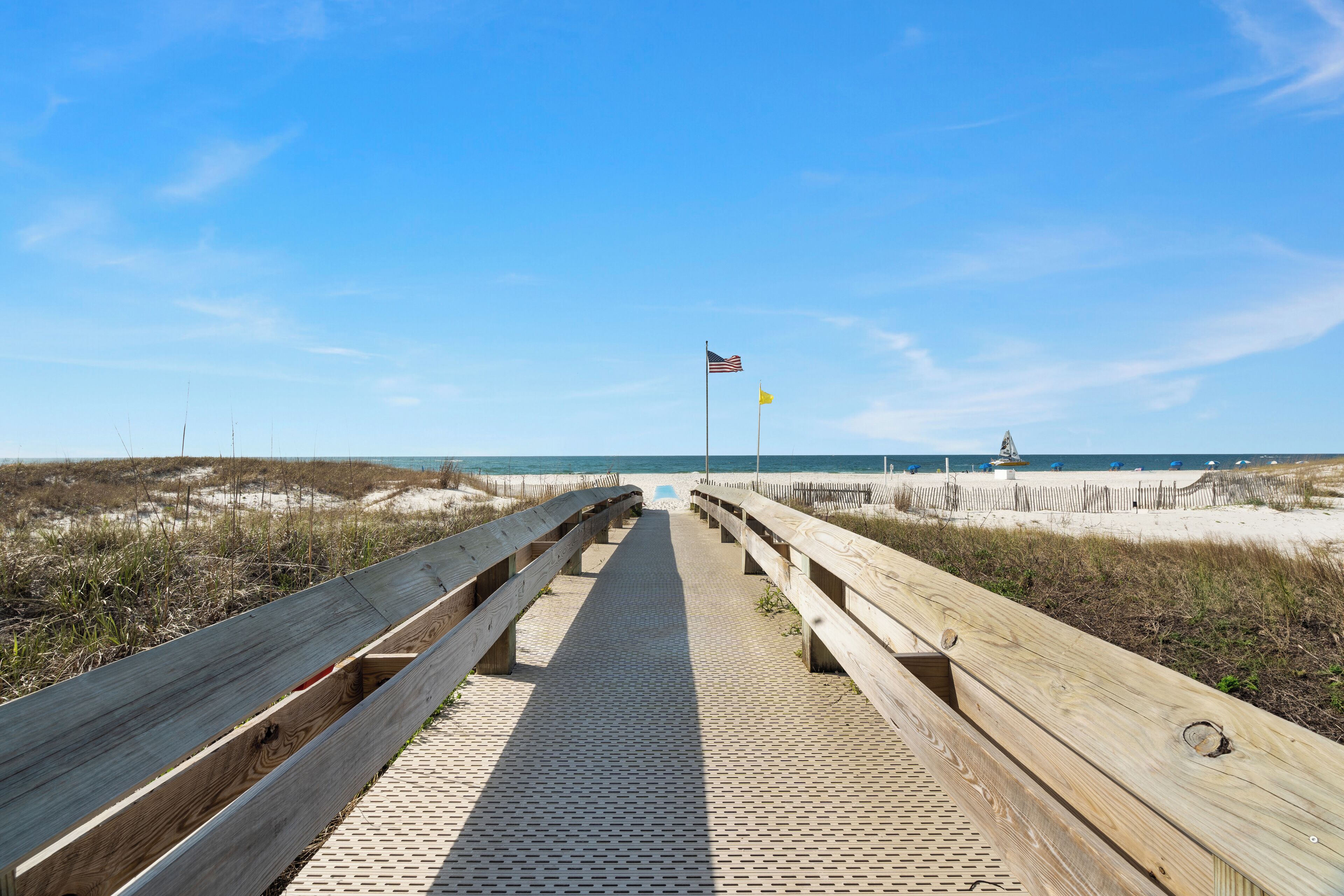 A wooden boardwalk leading to a beach with a sandy shore and a clear blue sky.