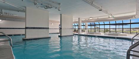 Una piscina interior con agua azul cristalina, paredes enlosadas y amplias ventanas que dejan entrar la luz natural.