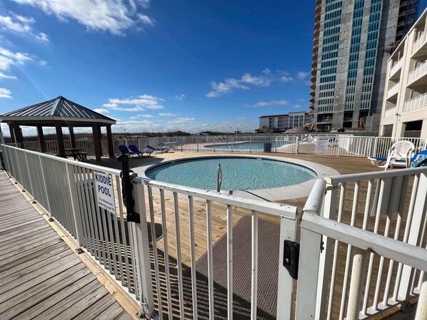 A pool area with a kiddie pool, lounge chairs, and a gazebo. - Sugar Beach 122 by ALBVR - Nice Studio Condo with New Sofa, AC and Smart TV (Orange Beach)