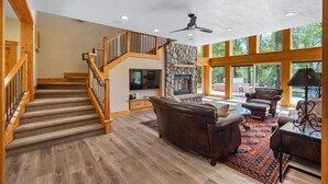 A spacious living area with a stone fireplace, wooden staircase, and large windows. - Riverfront, Hot Tub, Starlink Internet, Basketball! (Durango)