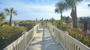 A wooden boardwalk leading to a gated entrance, surrounded by palm trees and shrubs. - Breakers 110 - 1st Floor Ocean Front Condo (Hilton Head Island)