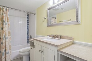 Une salle de bain avec des toilettes blanches, une baignoire, un lavabo avec un miroir et un rideau de douche.