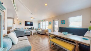 A spacious living room with a sofa, coffee table, and a dining area with a bench. - Pet Friendly, Boardwalk, Glimpse of Ocean from Deck (Port Aransas)