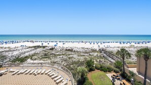 Une vue sur la plage, avec une zone de sable, des palmiers et une terrasse en bois équipée de chaises longues.