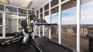 Une salle de sport équipée d’un tapis de course, d’un vélo elliptique et d’un vélo d’appartement, avec de grandes fenêtres donnant sur une piscine et un espace extérieur.