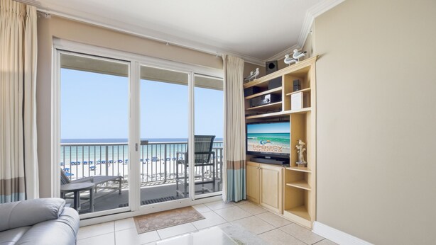 Un salon comprenant un canapé, un téléviseur à écran plat, un balcon avec vue sur la plage et un meuble de rangement en bois.