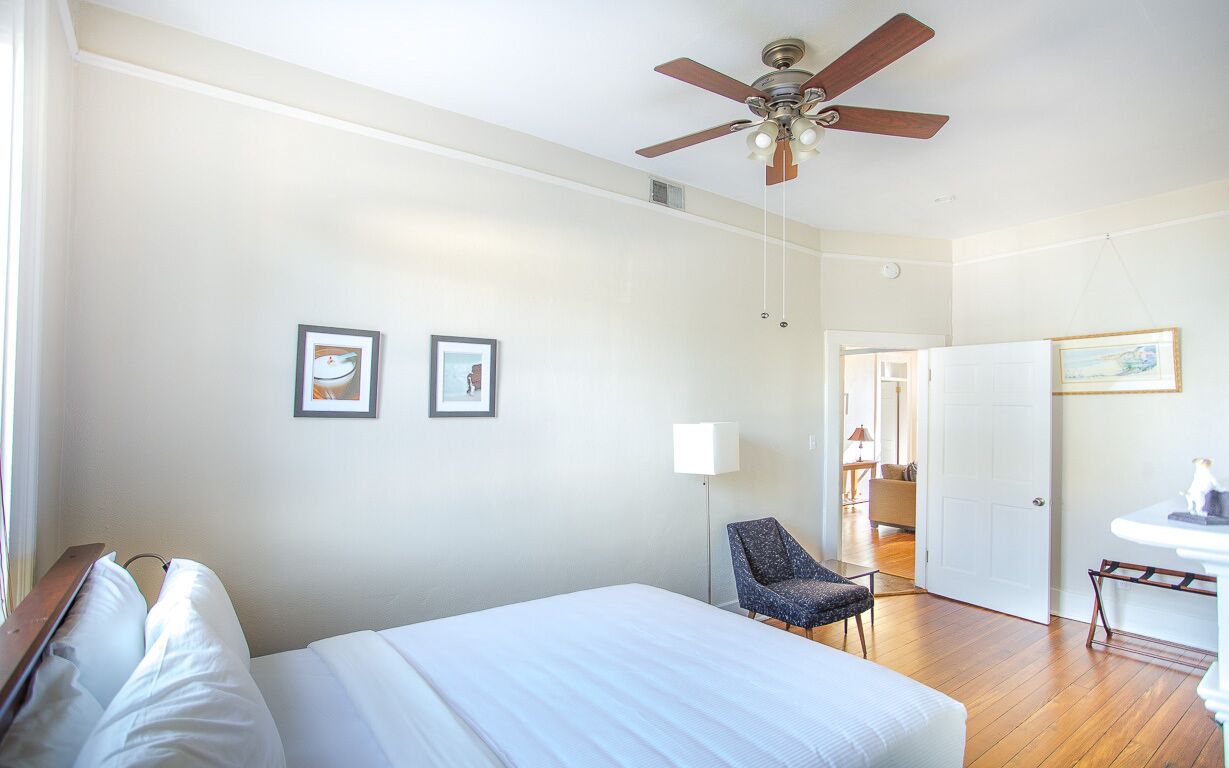 Quarto de hotel com cama, poltrona, escrivaninha e ventoinha no teto.