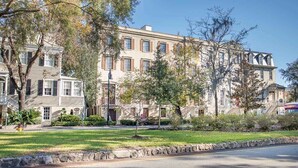 A row of multi-story residential buildings with a stone curb, a grassy lawn, and mature trees.
