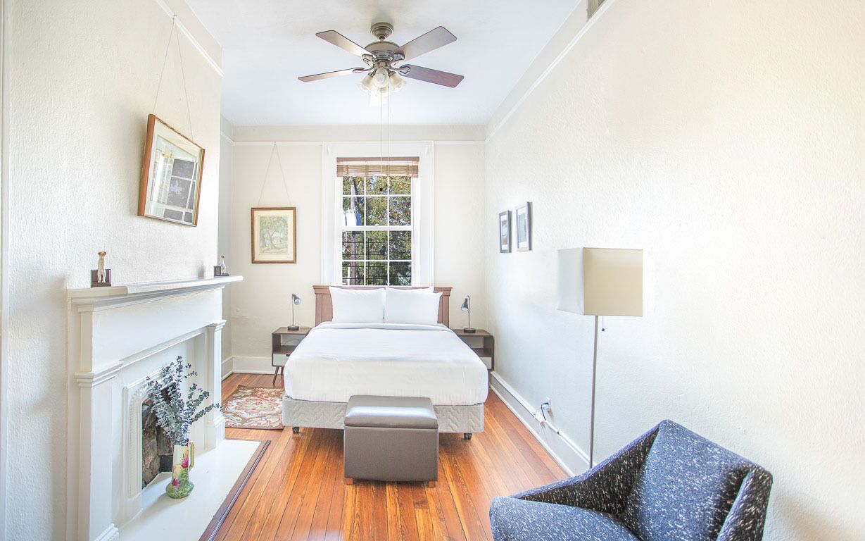 A bedroom with a bed, a chair, a fireplace, a ceiling fan, and a window.