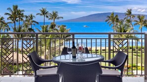 Ein Balkon mit Tisch und Stühlen mit Blick auf einen Strand, Palmen und den Ozean.