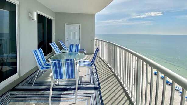 A balcony with a glass table and blue-striped chairs, overlooking a beach. - Island Royale P403 – Penthouse-Level Beachfront Luxury with Stunning Views (Gulf Shores)