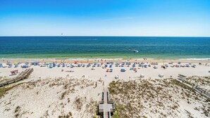 A beach with numerous umbrellas and sun loungers, a wooden boardwalk leading to the beach, and a clear view of the ocean. - Island Royale P403 – Penthouse-Level Beachfront Luxury with Stunning Views (Gulf Shores)